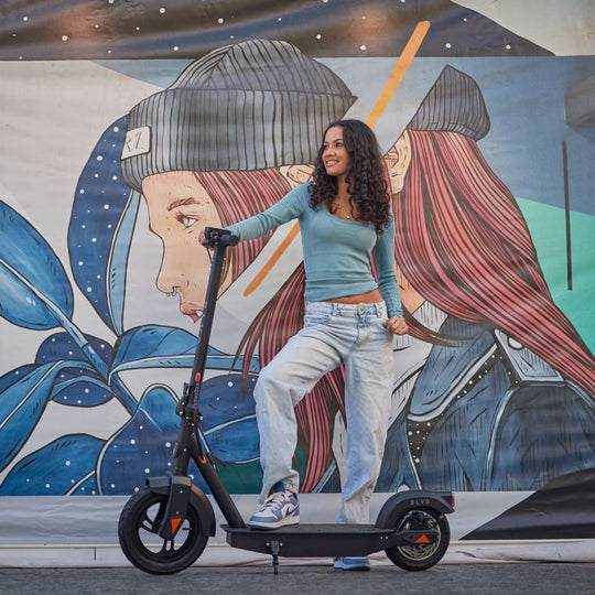 young female in casual street wear standing next to a blvd elite electric scooter in front of wall mural