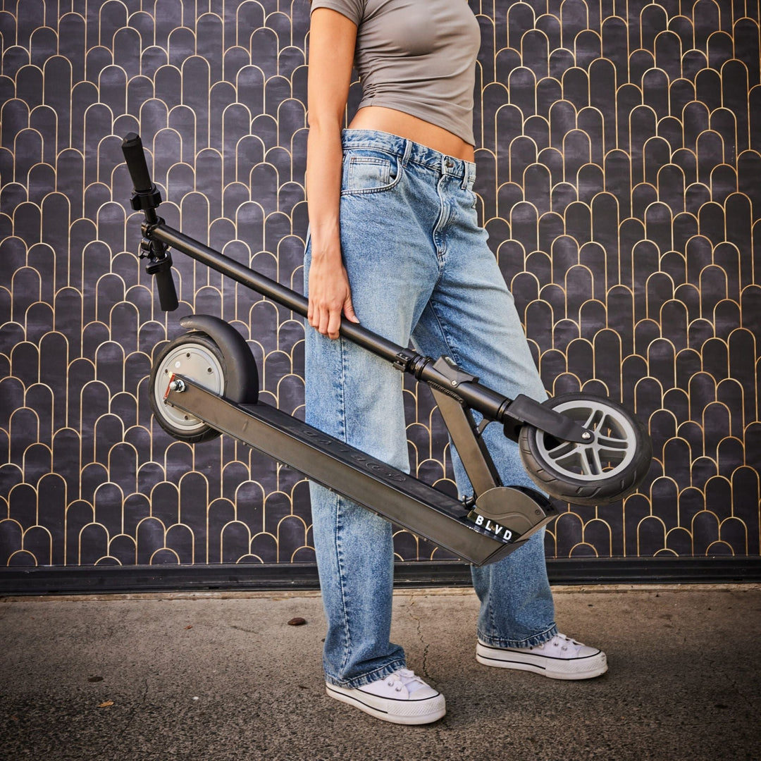 female holding a folded up blvd forge electric scooter in front of a black wall